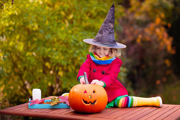 Child carving Halloween pumpkin. Kids carve pumpkins for trick or treat jack o lantern. Autumn activity for children. Little girl in scary witch costume and hat. Kid playing in autumn garden.