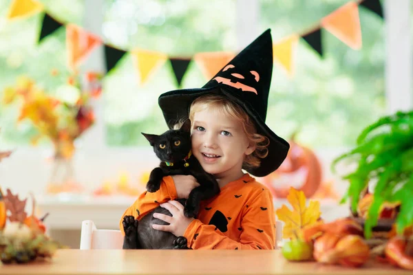 ハロウィンの衣装の子供 子供のトリックや治療 カボチャの提灯を持つ小さな男の子と黒猫 魔女の帽子と子猫の赤ちゃん 秋の季節の休日の装飾 秋の葉と家のお祝いのインテリア — ストック写真