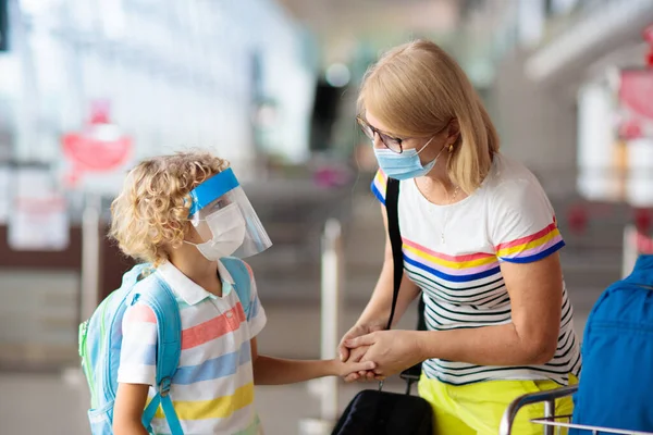 Family in airport in face mask and shield. Virus outbreak. Coronavirus and flu pandemic. Safe travel with young child and baby. Mother and kids boarding airplane in surgical masks.