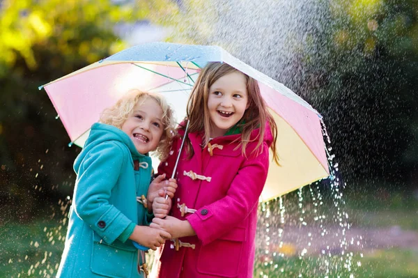 秋のシャワー雨の中で遊んでカラフルな傘を持つ子供たち 雨で公園で暖かいダッフルコート遊びの小さな男の子と女の子 子供のための屋外の楽しみを秋 雨を引く子供は — ストック写真