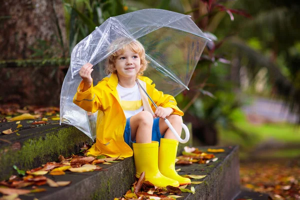 秋の雨の中で遊ぶ子供 傘を持ってる子供 秋の季節に公園を走る少年 どんな天気でも子供のための屋外の楽しみ 子供のための雨防水摩耗 ブーツやジャケット — ストック写真