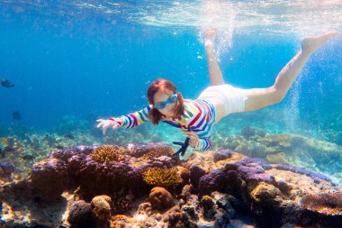 Çocuk şnorkelle yüzüyor. Çocuklar su altında yüzer. Çocuklarla plaj ve deniz tatili. Küçük kız mercan resifi balıklarını izliyor. Egzotik adada deniz yaşamı. Çocuk yüzüyor ve şnorkel ve maskeyle dalıyor..