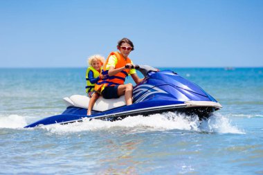 Jet ski 'deki aile. Genç bir çocuk ve küçük çocuklar su motosikletinde kayak yapıyor. Genç adam ve çocuklar tropikal denizde şahsi su araçlarında. Aktif yaz tatili. Spor ve okyanus aktiviteleri. Plaj tatili.