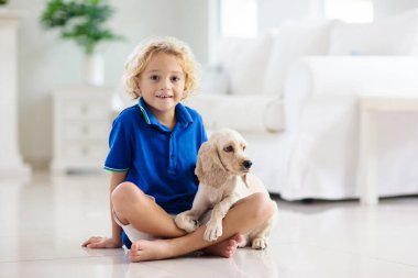 Çocuk yavru köpekle oynuyor. Çocuklar köpek yavrusuyla oynar. Küçük çocuk ve Amerikan cocker spaniel evdeki kanepede. Çocuklar ve evcil hayvanlar evde. Çocuk evcil hayvanıyla yerde oturuyor. Hayvan bakımı..