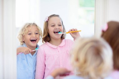 Dişlerini fırçalayan çocuk. Diş macunu ve fırçası olan çocuklar. Diş ve ağız temizliği, bakım. Çocuklar için sağlıklı günlük rutin. Çocuk duştan sonra veya evde banyo yaptıktan sonra. Diş macunlu pijamalı kız ve oğlan..