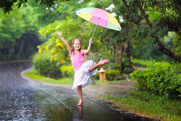 雨の中で遊んでいる子供 大雨の中 傘を差した子供たちが屋外で遊ぶ 少女は最初の春のシャワーに巻き込まれた 雨の秋の天気で子供たちの屋外の楽しみ 熱帯低気圧の中を走る子供 — ストック写真