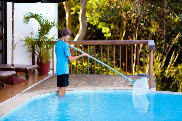Boy cleaning swimming pool. Maintenance and service for outdoor pool. Teenager after school job and house help. Teen student picking foliage leaf out of water. Garden and backyard chores.