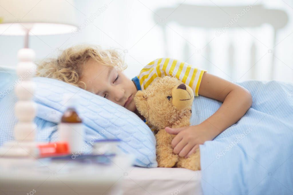 Sick little boy with asthma medicine. Ill child lying in bed. Unwell kid with chamber inhaler for cough treatment. Flu season. Bedroom or hospital room for young patient. Healthcare and medication.