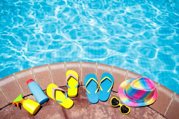 Swimming pool accessories flat lay. Top view of beach items on pool deck. Flip flops, bikini and hat, sun glasses. Water toys. Summer vacation in tropical resort. Copy space. Colorful beach wear.