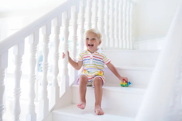 Kid walking stairs in white house. Baby boy playing in sunny staircase. Family moving into new home. Child crawling steps of modern stairway. Foyer and living room interior. Home safety for toddler.