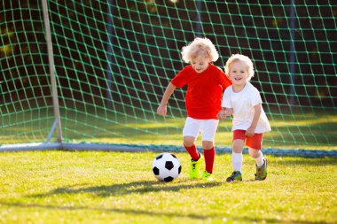 Çocuklar dışarıda futbol oynarlar. Çocuklar futbol maçında gol attılar. Küçük çocuk topa vuruyor. Formalı ve kramponlu koşan çocuk. Okul futbol kulübü. Genç oyuncu için spor eğitimi.
