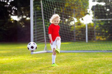 Çocuklar dışarıda futbol oynarlar. Çocuklar futbol maçında gol atıyor. Küçük çocuk topa vuruyor. Formalı ve kramponlu koşan çocuk. Okul futbol kulübü. Genç oyuncu için spor eğitimi.