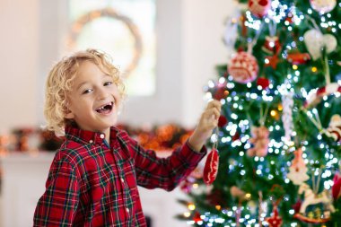 Evde Noel ağacı süsleyen çocuk. Xmas aksesuarlı, kareli gömlekli küçük çocuk. Çocuklu aile kış tatilini kutlar. Çocuklar Noel için oturma odasını ve şömineyi dekore ederler..