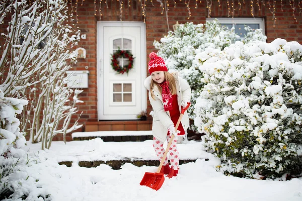 孩子们铲雪 冬天暴风雪过后 一个拿着铲子的小女孩正在清理车道 圣诞节暴风雪过后 孩子们清空了家门口的小路 降雪的乐趣 孩子们在冰冷寒冷的花园里玩耍 — 图库照片