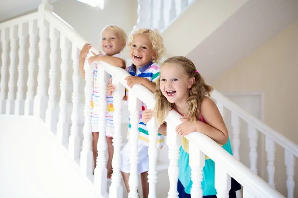 Kids walking stairs in white house. Children playing in sunny staircase. Family moving into new home. Boy and girl on steps of modern stairway. Foyer and living room interior. Child at stair case.
