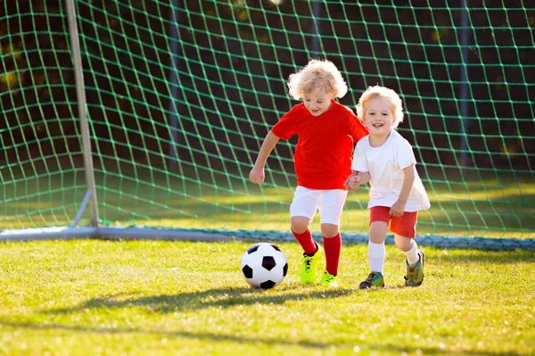 Kids play football on outdoor field. Children score a goal at soccer game. Little boy kicking ball. Running child in team jersey and cleats. School football club. Sports training for young player.