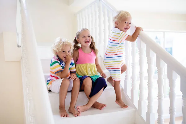 Kids walking stairs in white house. Children playing in sunny staircase. Family moving into new home. Boy and girl on steps of modern stairway. Foyer and living room interior. Child at stair case.