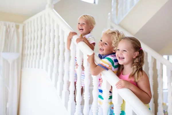 子供たちは白い家の階段を歩く 日当たりの良い階段で遊ぶ子供たち 家族は新しい家に移る 階段の近代的な手順で男の子と女の子 ホワイエとリビングルームのインテリア 階段の子 — ストック写真