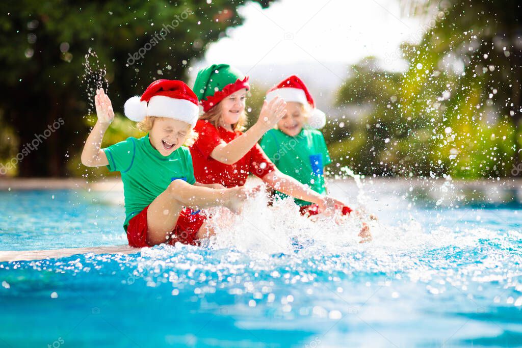 Christmas vacation on tropical island. Kids in Santa hat playing in swimming pool on family Xmas vacation. Winter holidays at the beach. Travel with children. Boy and girl swim. Merry Christmas card.