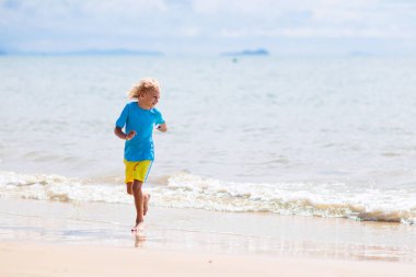 Tropik plajda oynayan çocuklar. Çocuklar yaz tatilinde yüzer ve denizde oynarlar. Kum ve su eğlencesi, küçük çocuklar için güneş koruması. Okyanus kıyısında koşan ve zıplayan küçük çocuk.