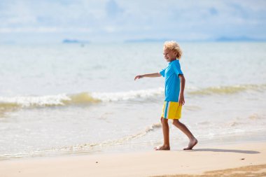 Tropik plajda oynayan çocuklar. Çocuklar yaz tatilinde yüzer ve denizde oynarlar. Kum ve su eğlencesi, küçük çocuklar için güneş koruması. Okyanus kıyısında koşan ve zıplayan küçük çocuk.