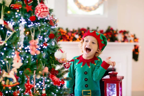 自宅でクリスマスツリーを飾る子供 自己の衣装やXmasの装飾付きの帽子の小さな男の子 子供たちと家族は冬の休日を祝います 子供たちはクリスマスのためにリビングルームと暖炉を飾る — ストック写真