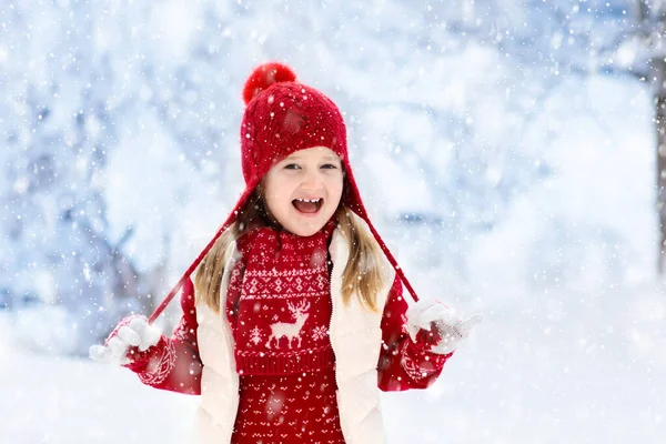 クリスマス休暇に雪の中で遊ぶ赤い帽子の子供 冬の屋外の楽しみ Xmas Eveの雪の公園で子供たちが遊ぶ ニットセーター スカーフの女の子とクリスマスの装飾でミトン — ストック写真