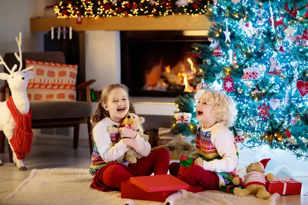 クリスマスツリーの子供たちとクリスマスの前夜の暖炉 自宅でクリスマスを祝う子供たちと家族 夏の木やオープニングプレゼントを飾るパジャマを着た男の子と女の子 子供のための休日の贈り物 — ストック写真