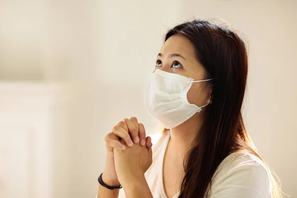 Pray for coronavirus victim. Asian woman in face mask praying for sick. Patient in hospital chapel or church during Covid-19 outbreak. Virus pandemic. People worship. Doctor saying a prayer.