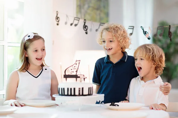 Music and piano theme kids birthday party. Kid with black and white cake. Child blowing candles and opening present. Little boy celebrating birthday. Event for young pianist. Festive decoration.