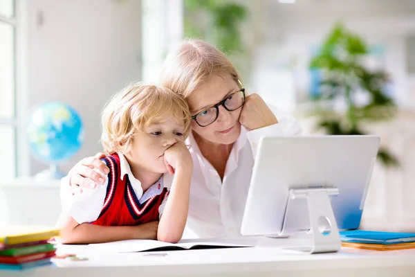 Online remote learning. School kids with computer having video conference chat with teacher and class group. Mother helping son. Child studying from home. Homeschooling in coronavirus outbreak.