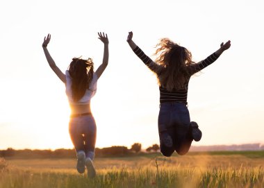 İki kız gün batımında tarlada atlıyor.