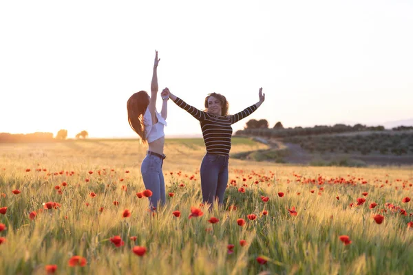 two girls jumping at sunset in the poppy field