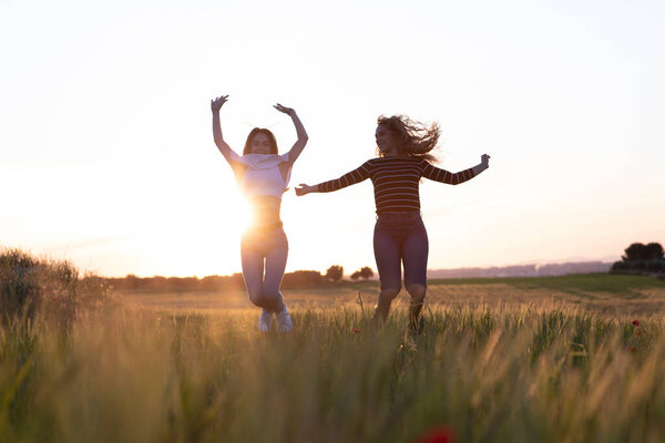 two girls jumping at sunset in the field