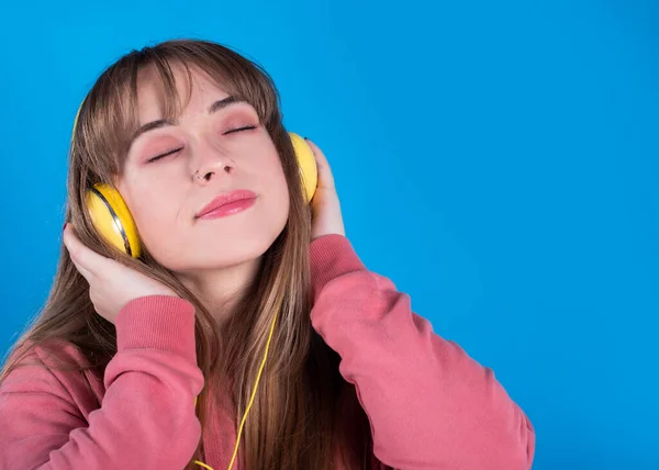一个年轻貌美的女人 用闭着眼睛 背景是蓝色的耳机听音乐 — 图库照片