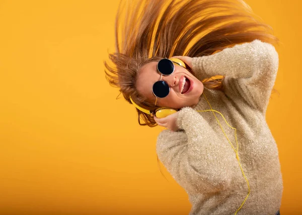 一位年轻貌美的女士带着耳机和太阳镜听音乐 她的头发在飘扬 背景是黄色的 — 图库照片