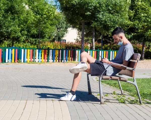 Sağlık maskeli genç bir adam parkta oturuyor.