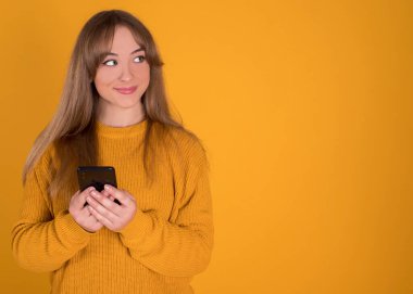 Akıllı telefonuyla müzik dinleyen genç kız sarı arka plandaki kulaklıklardan memnun.