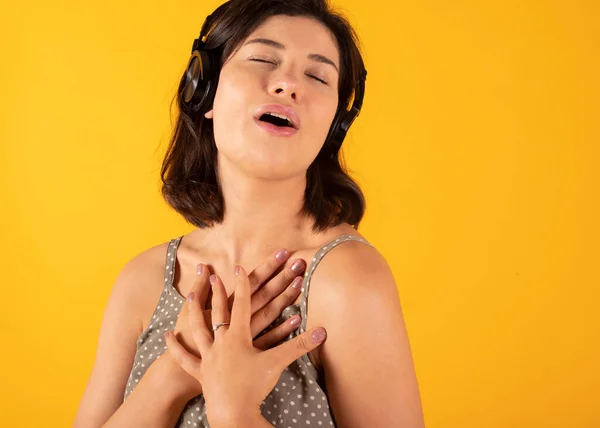 听音乐的女人带着耳机唱歌 背景是黄色的 — 图库照片