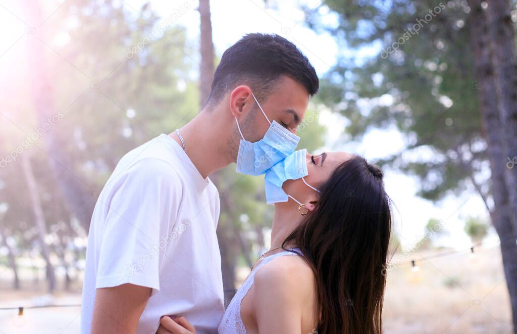 Young couple kissing with black protective masks. Pandemic. Coronavirus. A man and a girl kiss through a medical mask. Covid 19. Summer 2020. Kiss.
