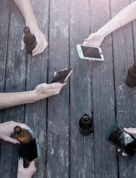 people hands with smartphone and beers on a wooden table