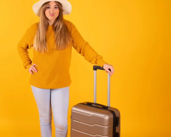 woman with a suitcase and a hat, travel concept, yellow background