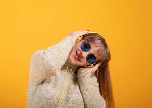 戴眼镜和耳机的女人听黄色背景的音乐 — 图库照片