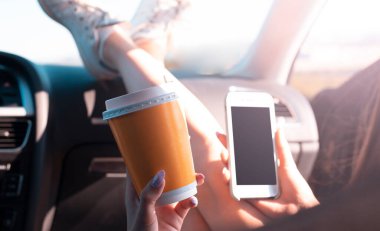 Bir kadının elinde kahve ve cep telefonu var.