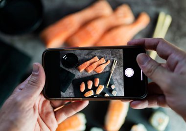 Eller cep telefonuyla Asyalı yemek suşisinin fotoğraflarını çekiyor.