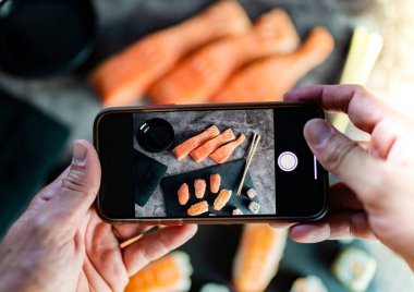 Eller cep telefonuyla Asyalı yemek suşisinin fotoğraflarını çekiyor.