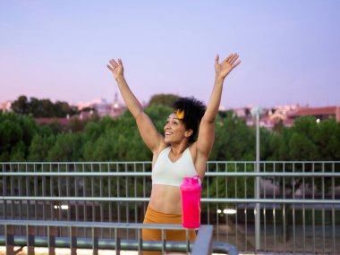 Siyah kadın, sporda kaybettiği gücü ve besinleri geri kazanmak için parkta antrenman yaptıktan sonra protein içer.