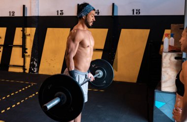 Çekici genç adam spor salonunda ağırlık kaldırıyor.