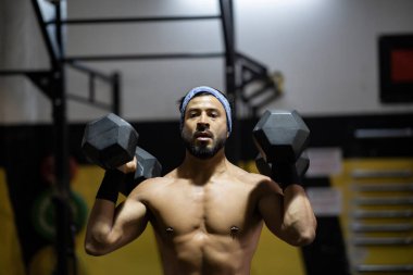 Çekici genç adam spor salonunda ağırlık kaldırıyor.