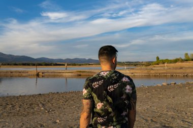 Arkadan poz veren, çiçek desenli gömlekli çekici bir genç.